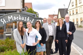 Eine Gruppe von acht Frauen und Männern steht vor dem Schild mit Aufschrift "St. Markushof".
