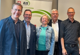 Vier Männer und in der Mitte eine Frau stehen vor einem Banner der KJS