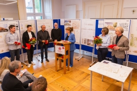 Sieben Personen stehen vor einigen Schautafeln mit Bauplänen.