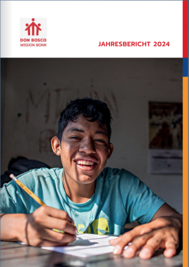 Ein südamerikanischer Junge sitzt an einem Tisch mit einem Bleistift in der rechten Hand. Auf dem Tisch liegt ein Blatt Papier.