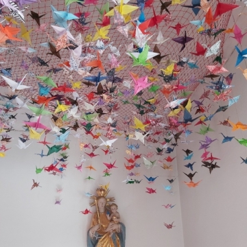 Über einer Marienstatue hängen viele Papier-Kraniche in einem Netz