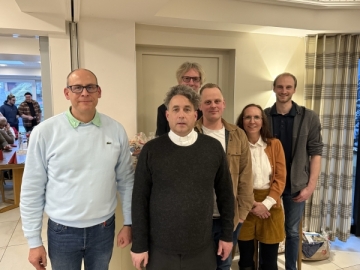 Fünf Männer und eine Frau stehen für ein Gruppenbild in einem Flur.