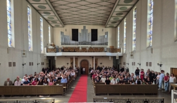 In einer Kirche sind die Kirchenbänke mit Menschen gefüllt, im Hintergrund ist die Orgel zu sehen