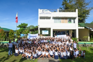 Philippinische Schülerinnen und Schüler stehen vor der neu gebauten taifunsicheren Schule und halten ein Dankesschild hoch.