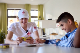 Luke Kelly sitzt mit einem Jugendlichen am Tisch und spielt ein Kartenspiel.
