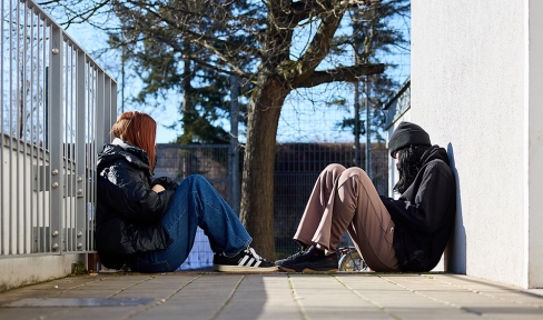 Zwei obdachlose Mädchen sitzen auf dem Boden einander gegenüber.