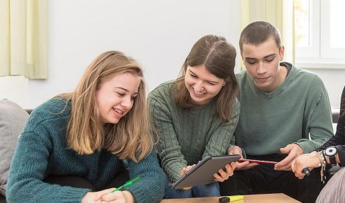 Jugendliche lachend und redend mit Tablet und Notizblock auf Sofa