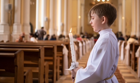 Junge mit Kommunionkerte und weißem Gewand in einer Kirche.