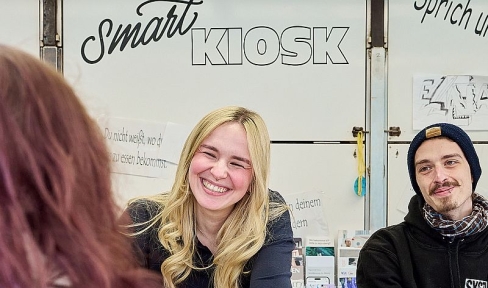 Eine Betreuerin und ein Betreuer im Gespräch mit einer Besucherin am Smart Kiosk von Don Bosco Nürnberg