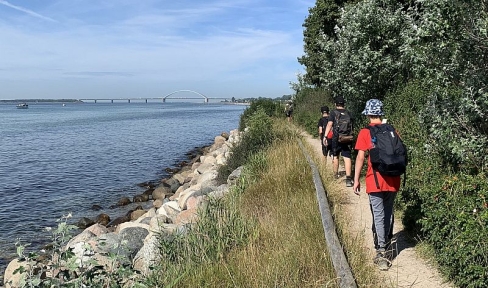 Jugendliche mit Rucksäcken gehen schmalen Wanderweg am Wasser entlang